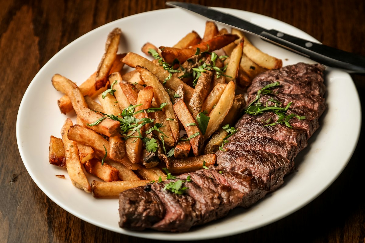 Sliced steak with fries on a white plate